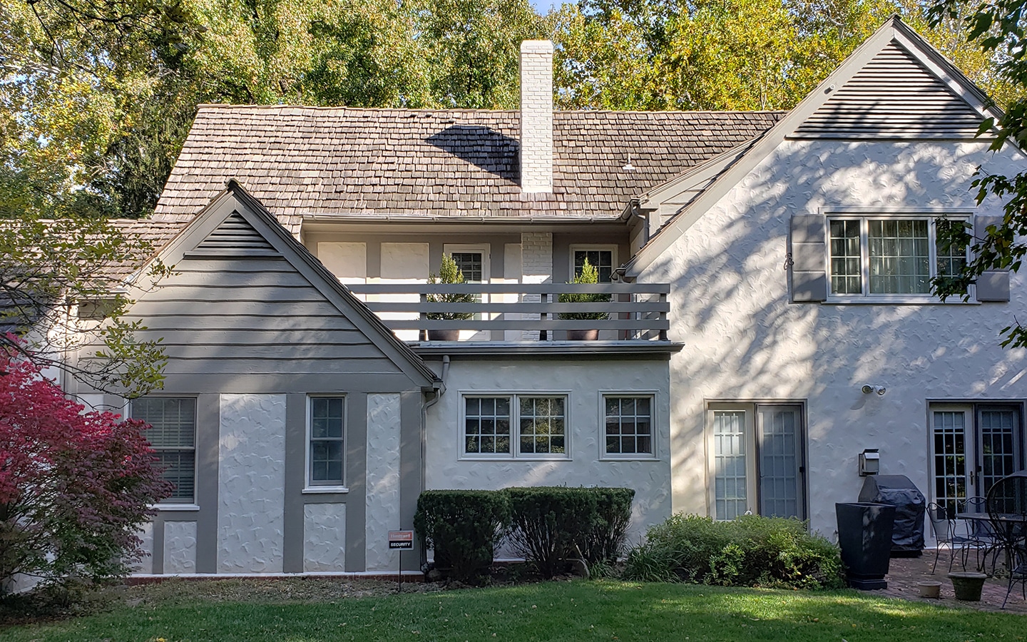 Rear exterior of a stucco home painted soft white with gray trim and a wood balcony railing - Mission Hills KS